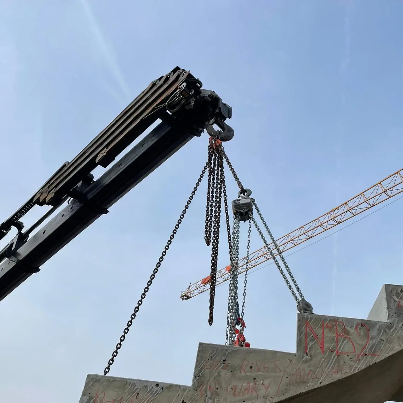 Charge suspendue par des chaînes à une grue, sur un chantier